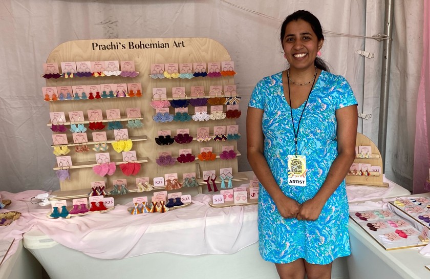 Smiling woman stands in front of a display of handmade earrings