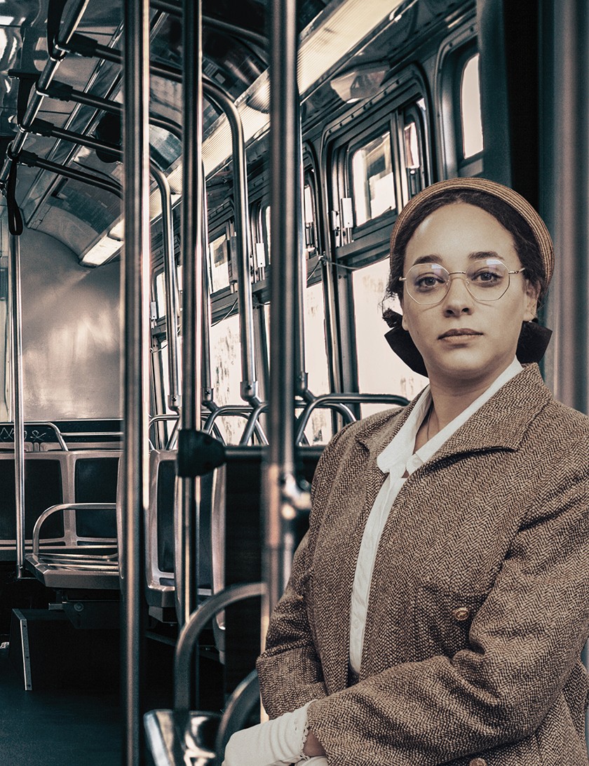 A sepia-toned photograph of a woman dressed in old fashioned clothing sitting inside a bus