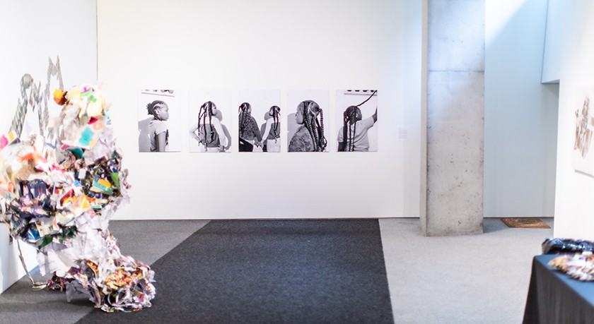 Five black-and-white photos hang on a white wall in front of an art gallery