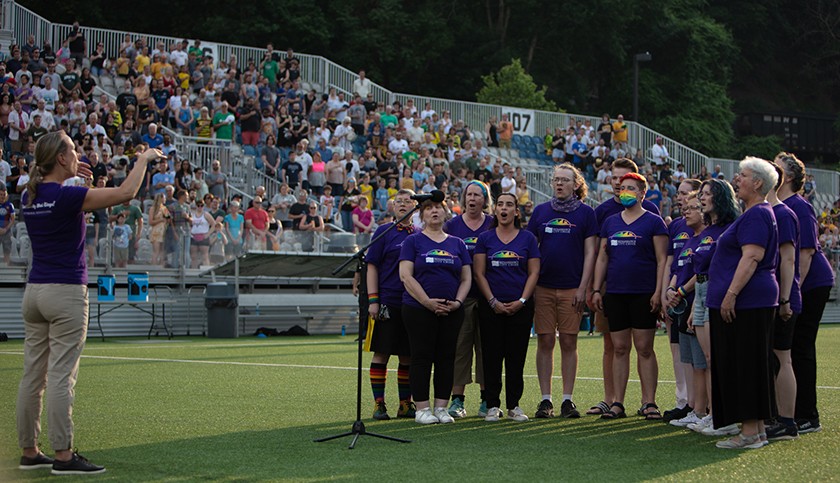 A group of people wearing purple T-shirts stand in front of a microphone on a soccer field