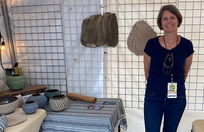 Smiling woman stands in booth next to a table of pottery