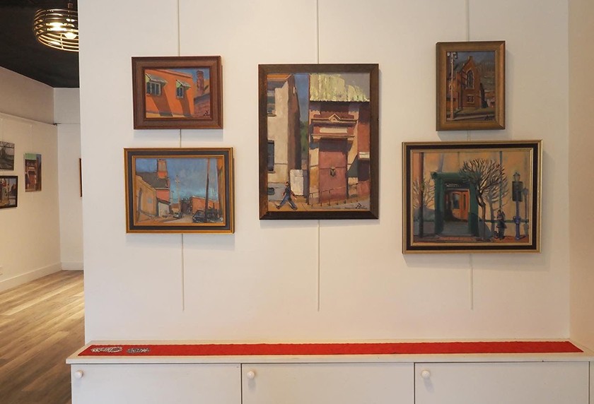 An exhibit wall showcasing five framed paintings of buildings