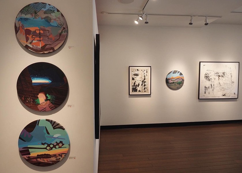 Artwork displayed on gallery walls including three circle-shaped paintings in the foreground and various sized pieces on a background wall