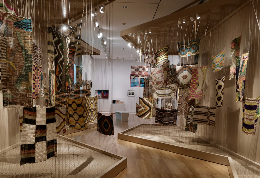Colorful woven textiles with geometric patterns hanging in a modern art gallery display.