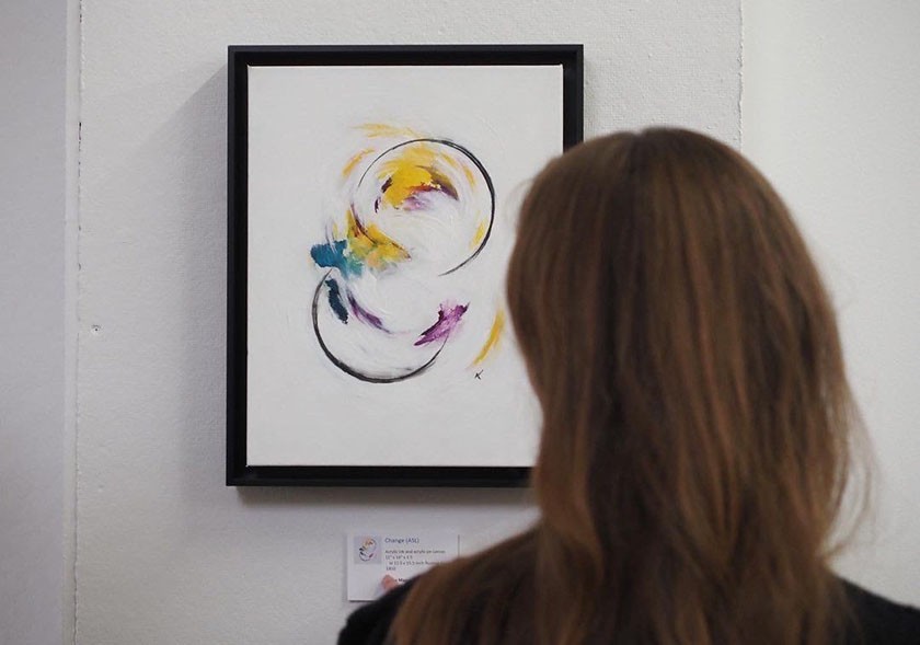 The back of a person's head as they look at a framed colorful artwork hanging on a wall
