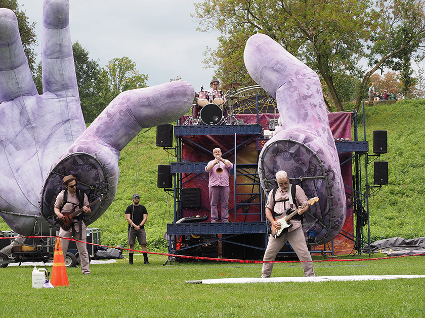 Musicians perform in front of sculptures of gigantic purple hands