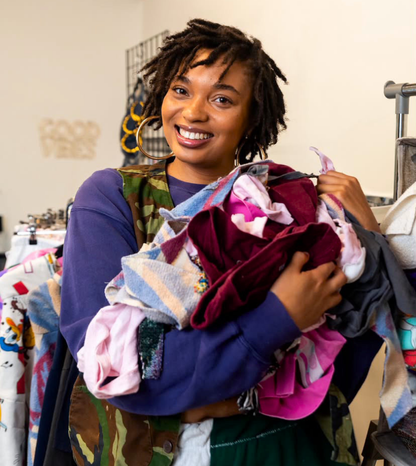 Smiling person holding a large pile of colorful clothing in a store setting.