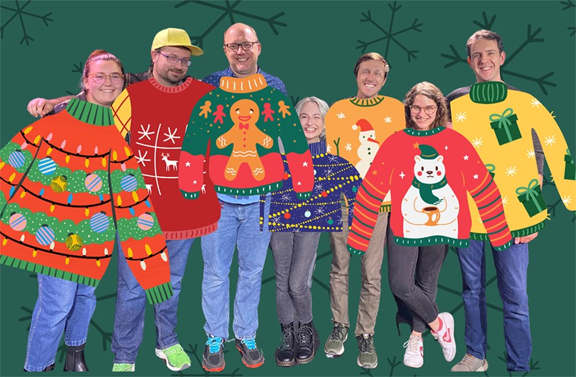 Seven smiling people pose for a portrait. Cartoon images of Christmas sweaters have been Photoshopped on top of each of them. The background is a green wall with snowflakes