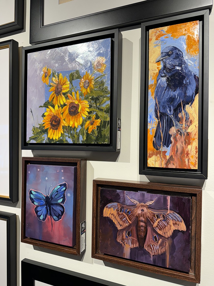 Assortment of framed paintings hanging on a wall. Paintings include images of sunflowers, birds, and butterflies