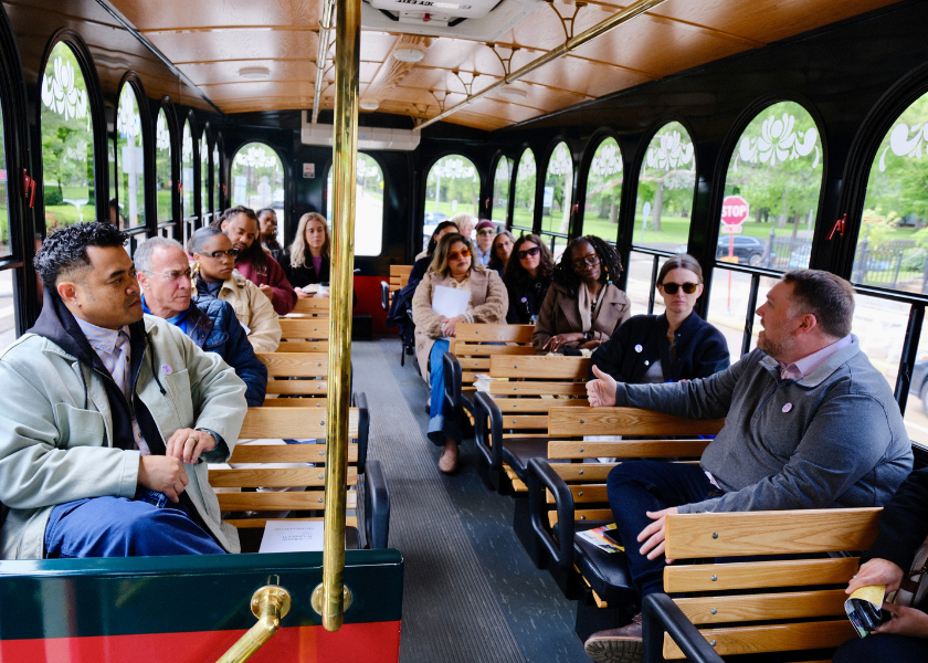 A group of people sit and talk inside a vintage-style trolley with wooden seats.