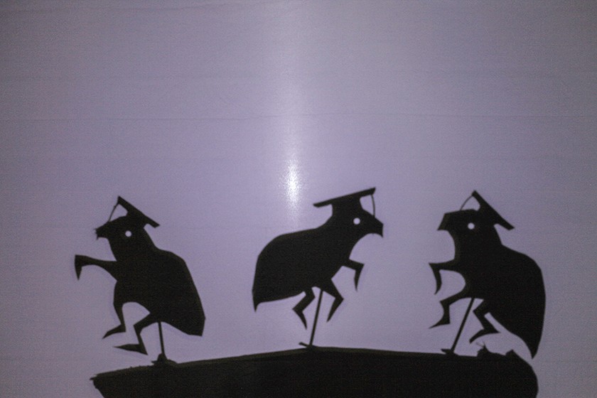 Dark silhouettes of flea-shaped puppets wearing graduation hats