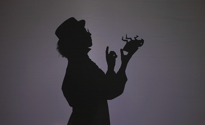 A dark silhouette of a human wearing a hat holding a dead flea