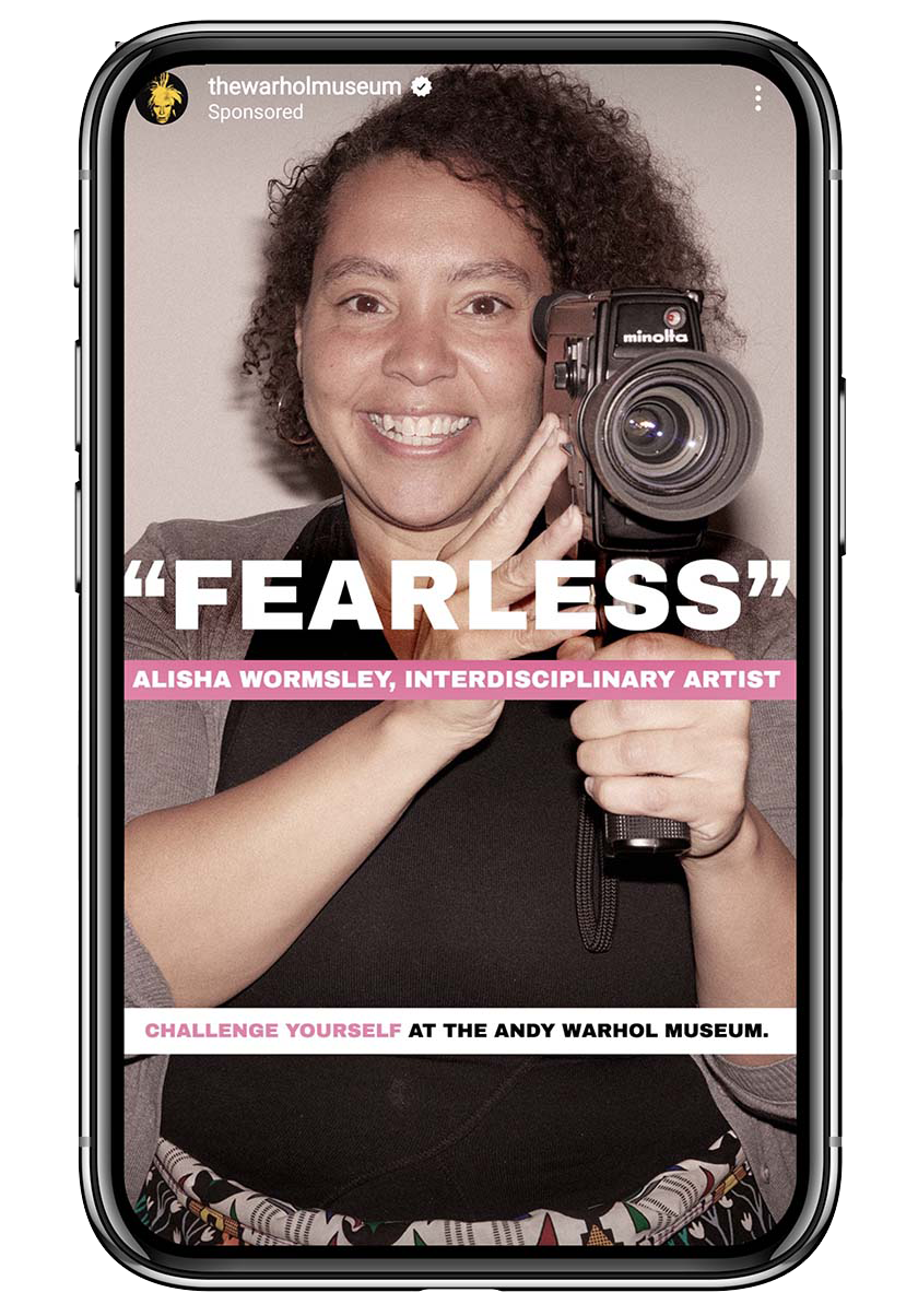 A phone screen showing a photograph of a smiling Black woman holding up a camera. The word "Fearless" is written across the image