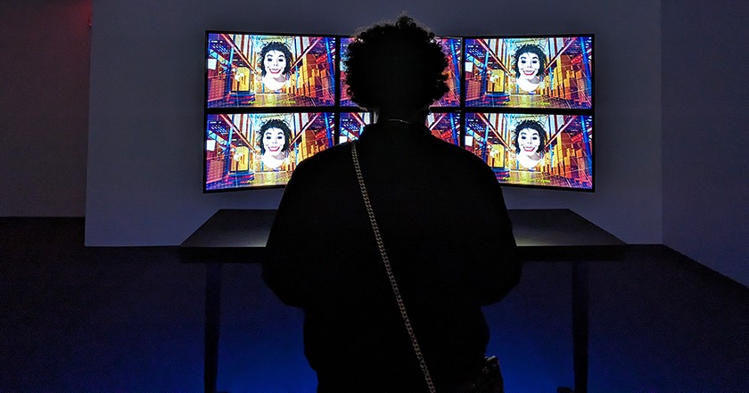 A silhouette of a woman looking at brightly colored tv screens showing a distorted Michael Jackson-esque figure