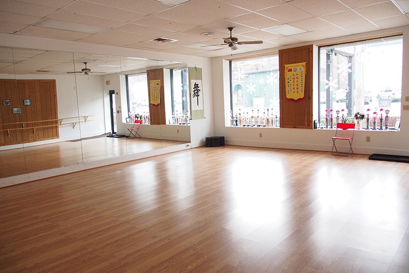 An empty performance studio with wood floors, floor-to-ceiling mirrors, and Asian artwork hanging on the walls