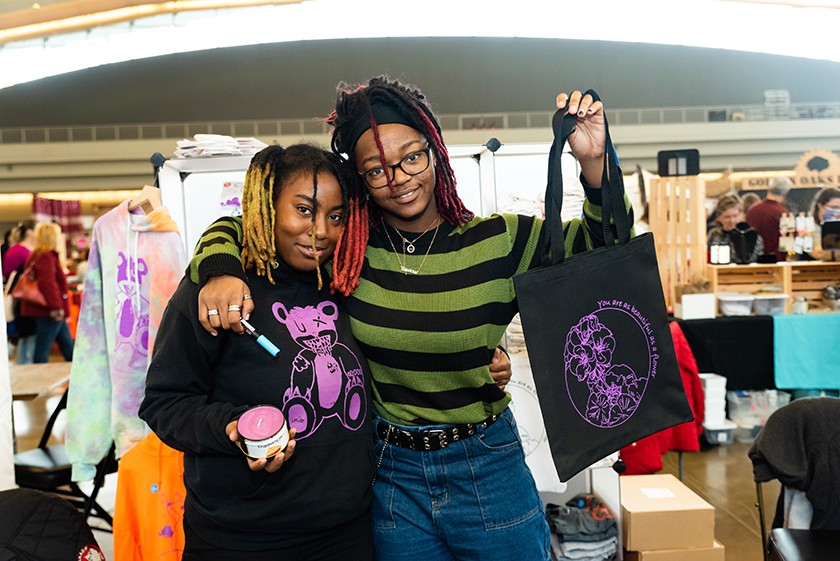 Two smiling Black youthmakers display handmade wares at Handmade Arcade's Holiday Market