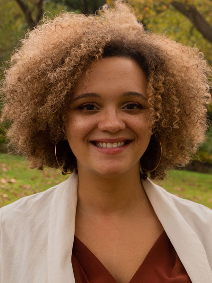 Person with short curly brown hair smiles for the camera