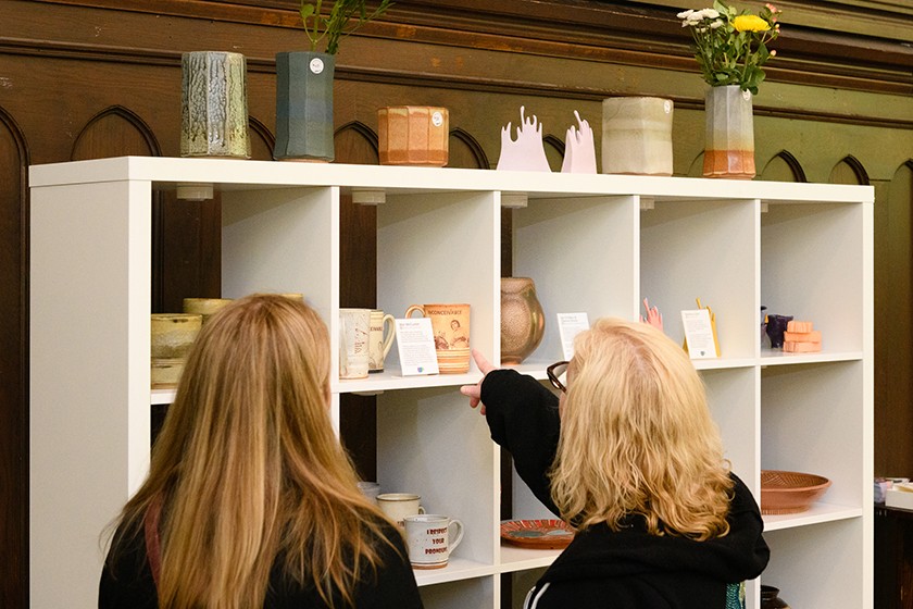 Two people look at pottery displayed on a white shelf
